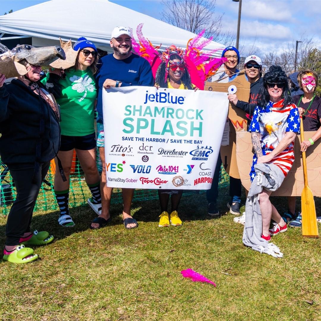 Group of people in costume holding jetBlue Shamrock Splash sign on the grass